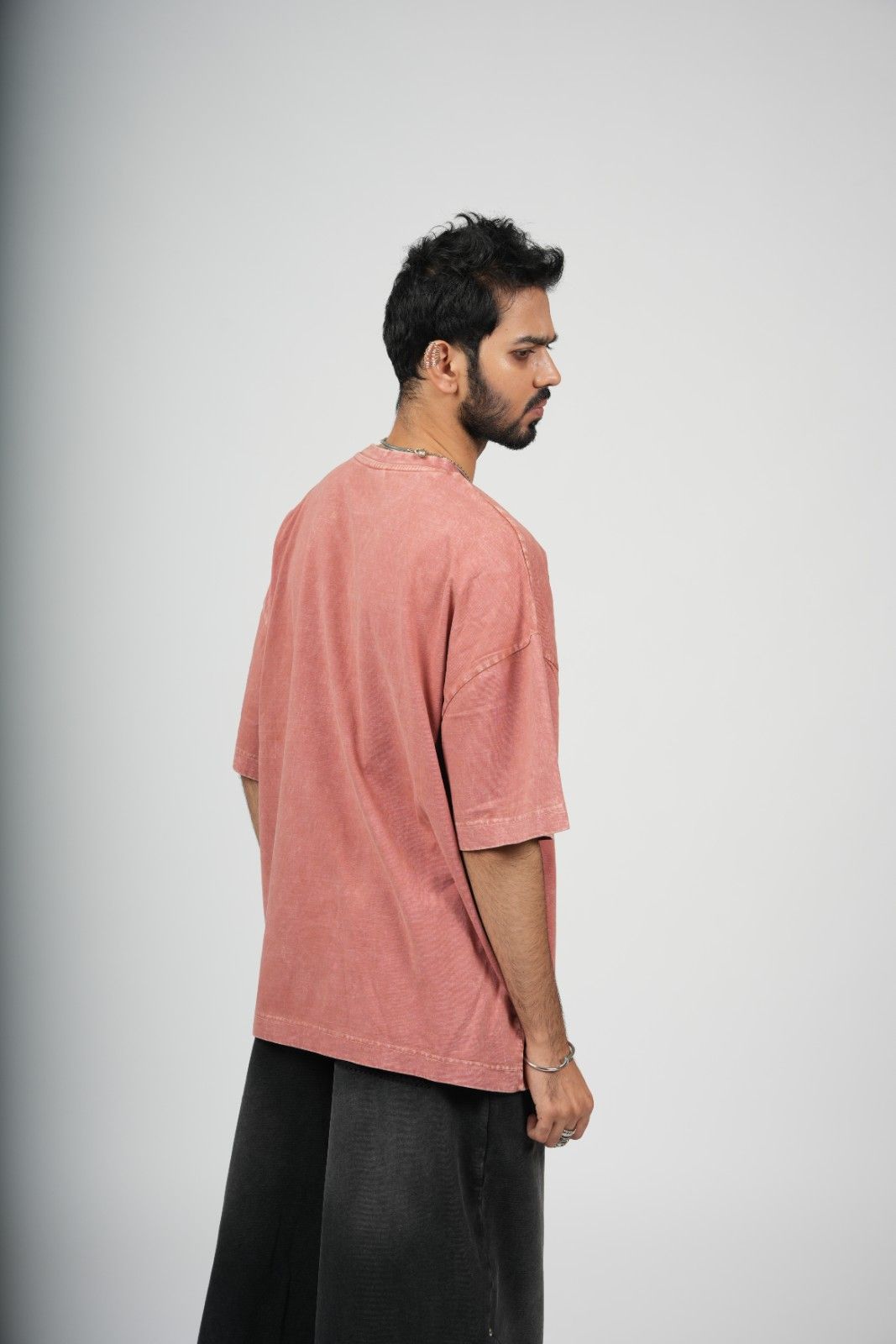 Man wearing a pink t-shirt and black pants on a gray background