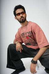 Man wearing a pink t-shirt with text and graphics, black pants, and sunglasses on a white background