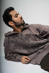 Man wearing a brown hoodie with intricate patterns on a gray background
