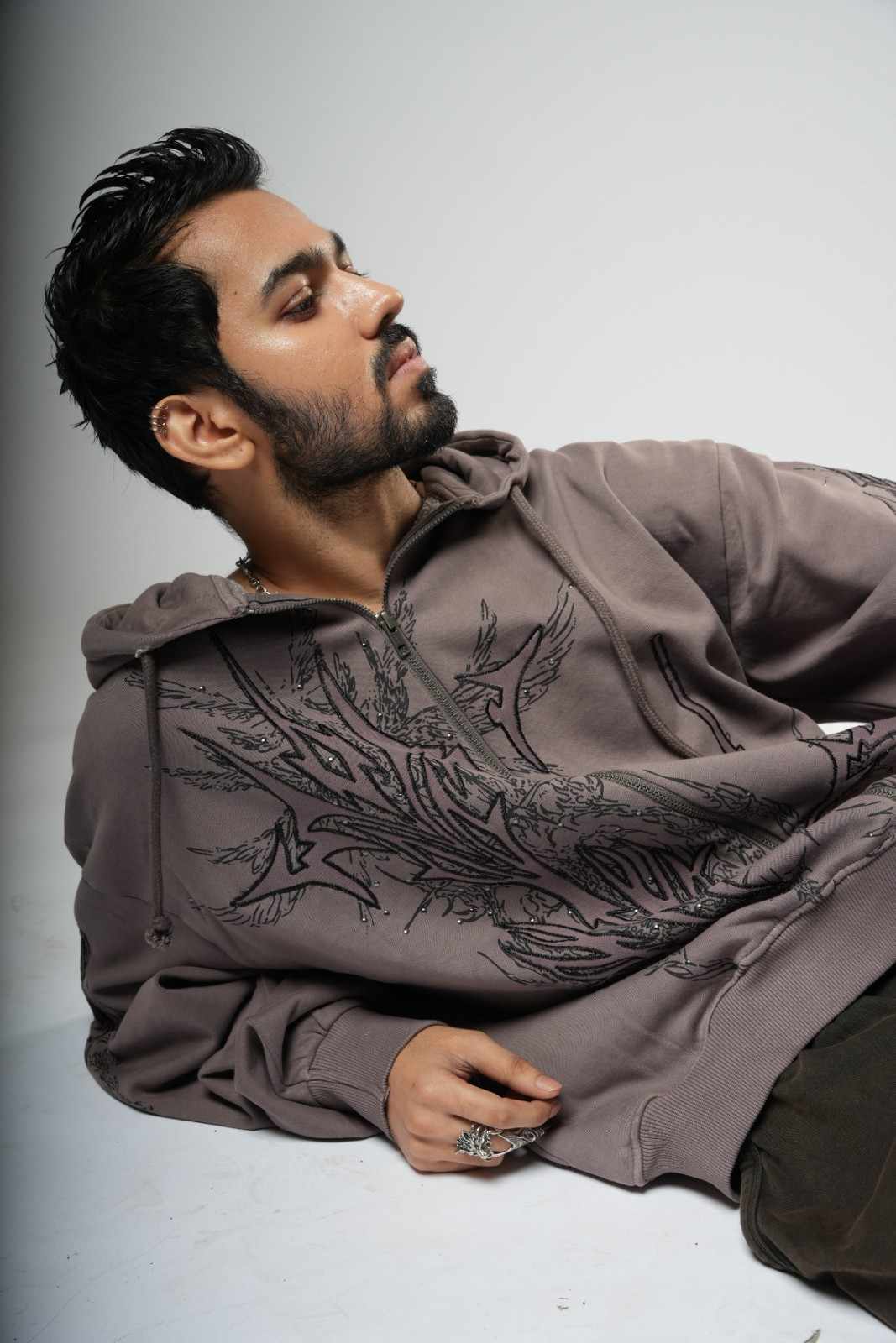 Man wearing a brown hoodie with intricate patterns on a gray background