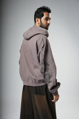 Man wearing a gray hoodie with intricate designs on a plain background