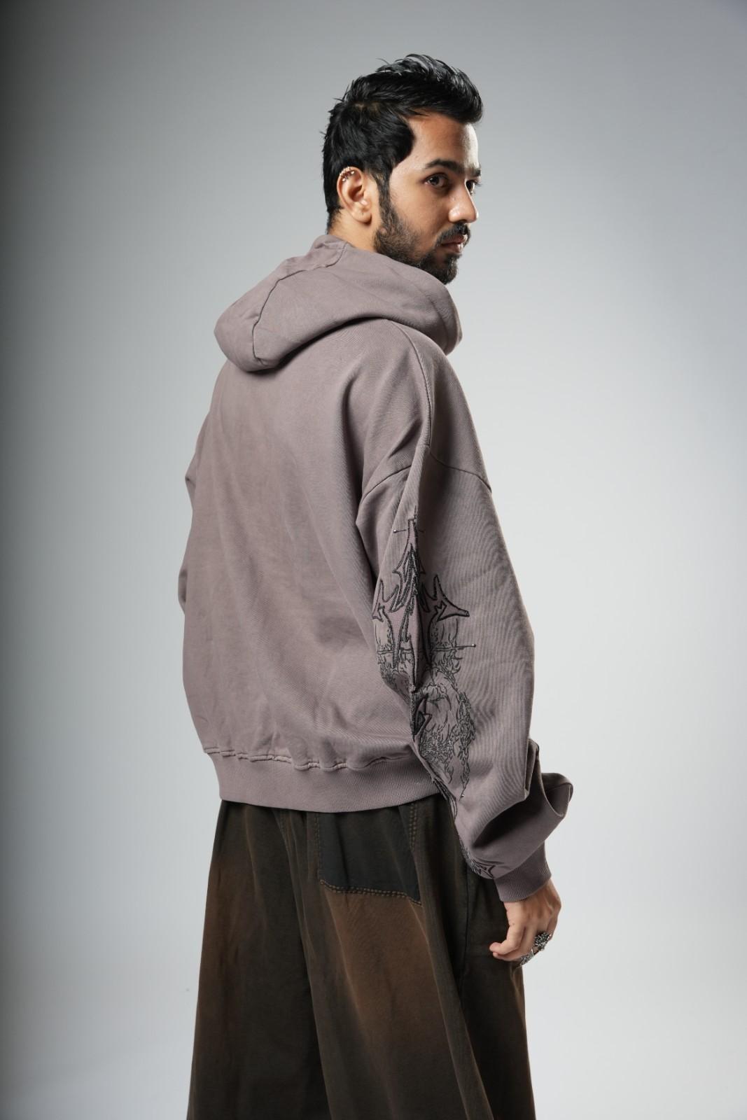 Man wearing a gray hoodie with intricate designs on a plain background