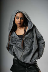 Person wearing a gray hooded jacket with braided hair on a gray background