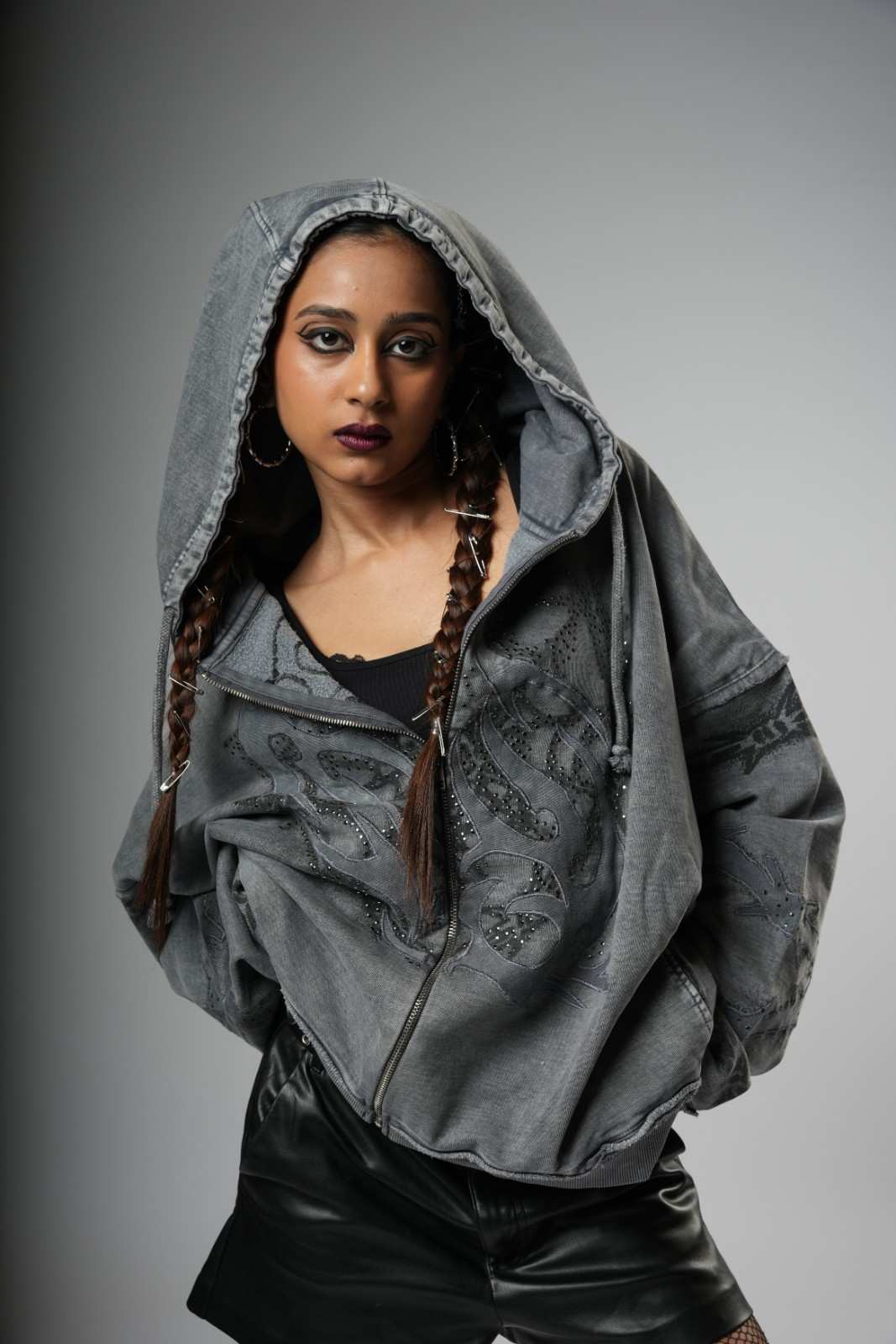 Person wearing a gray hooded jacket with braided hair on a gray background
