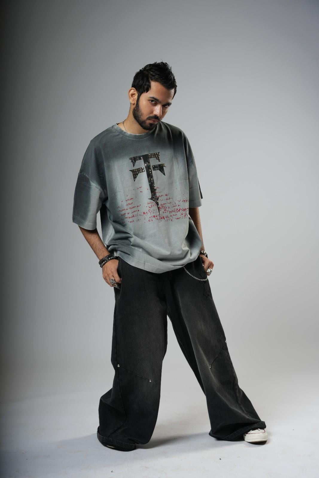 Man wearing a gray oversized sweater with a graphic design on a plain background