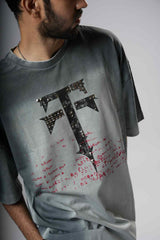 Person wearing a gray t-shirt with a large black letter 'TT' design on a plain background