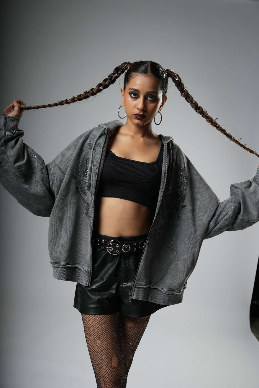 Person wearing a gray hoodie, black top, and shorts with fishnet stockings against a gray background