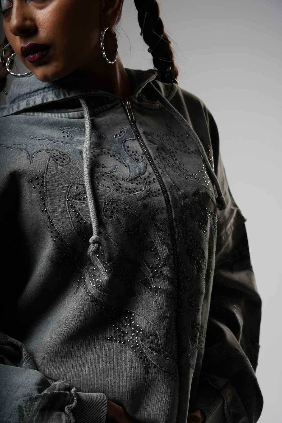 Person wearing a dark gray hoodie with intricate designs on a plain background