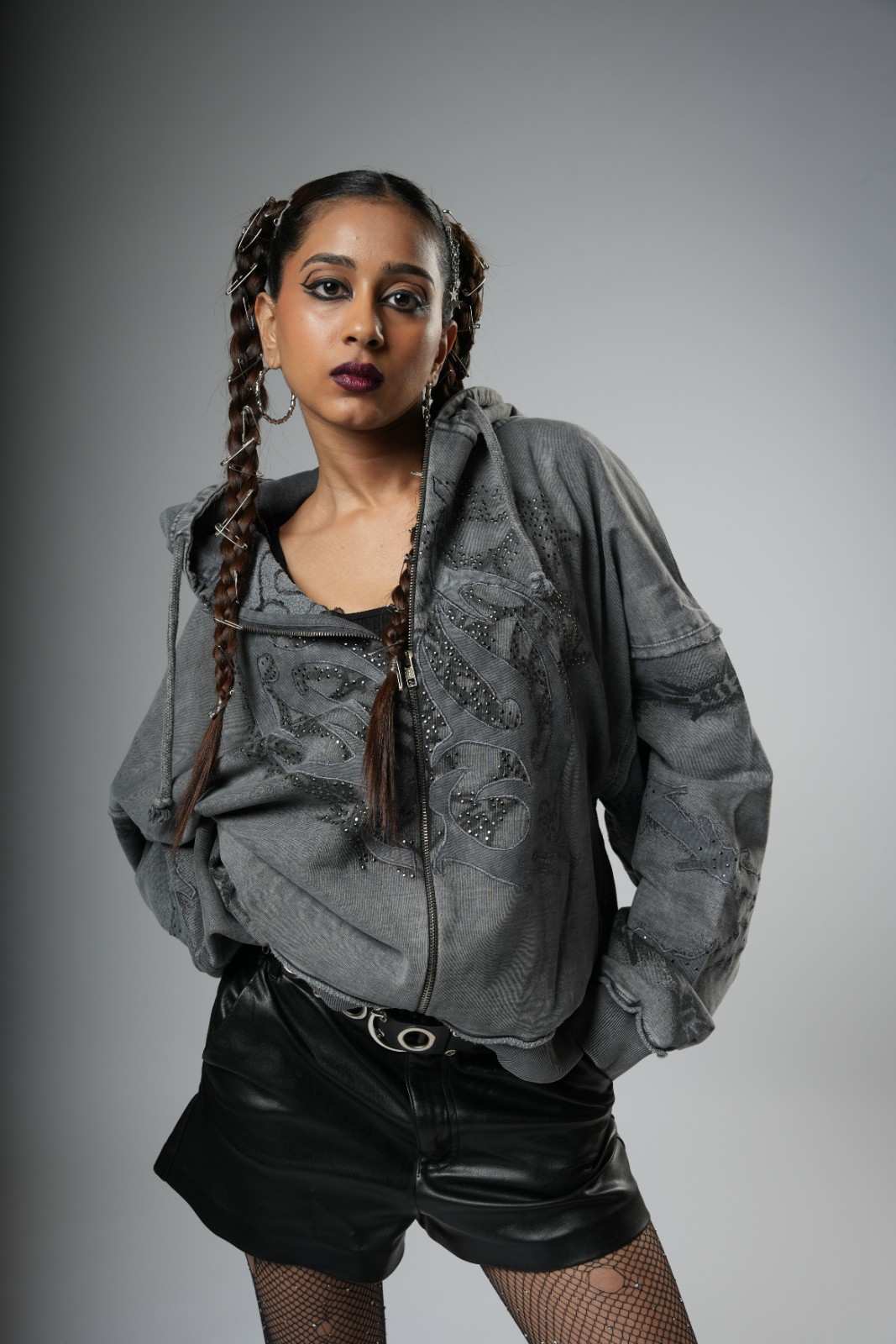Woman wearing a gray textured jacket and black leather shorts on a gray background