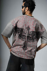 Person wearing a t-shirt with a cross and wings design on the back, standing against a gray background.