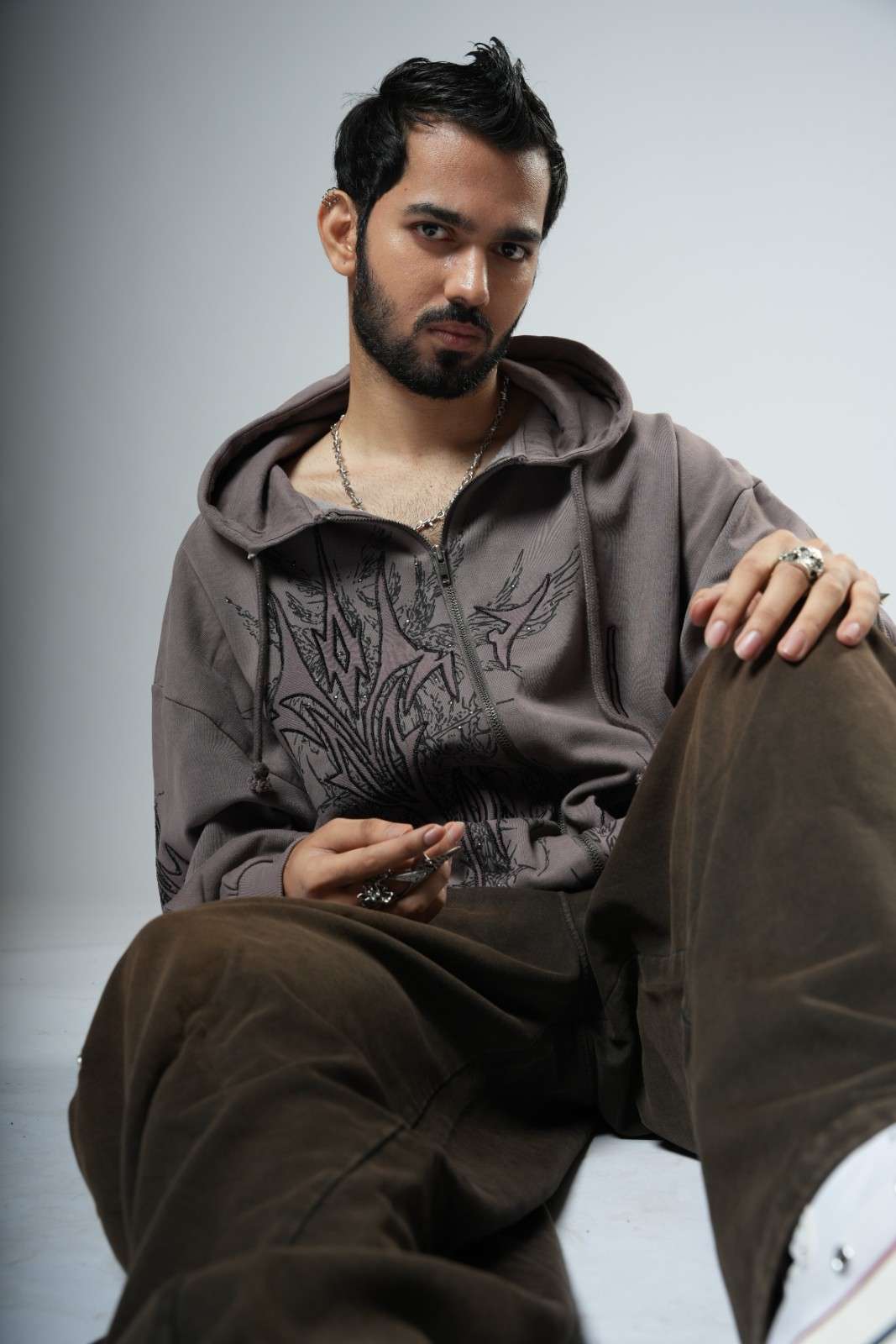 Man wearing a brown hoodie and pants sitting on a light gray background