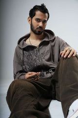 Man wearing a brown hoodie and pants sitting on a light gray background
