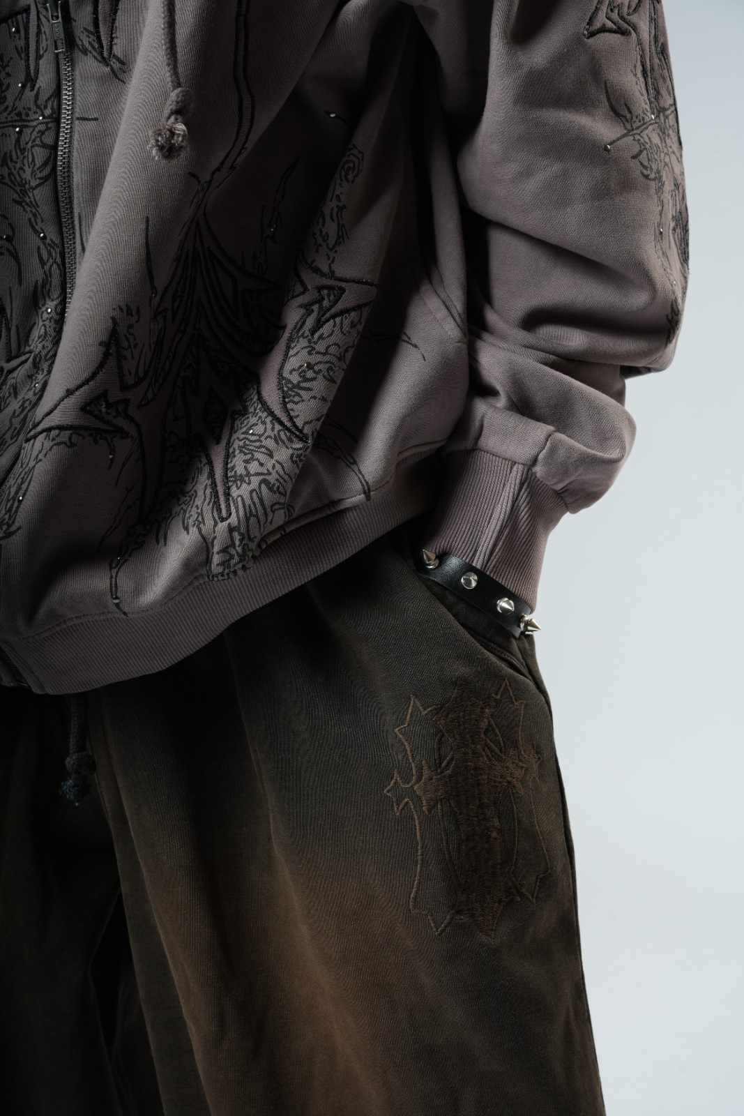 Person wearing a dark jacket and pants with embroidered designs on a neutral background