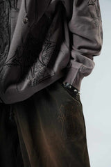 Person wearing a dark jacket and pants with embroidered designs on a neutral background
