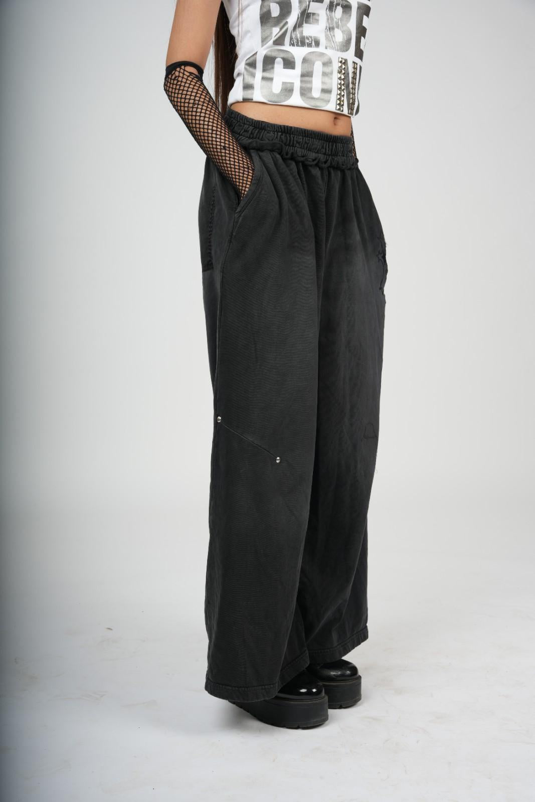 Person wearing black wide-leg pants and a white crop top with text on a plain background