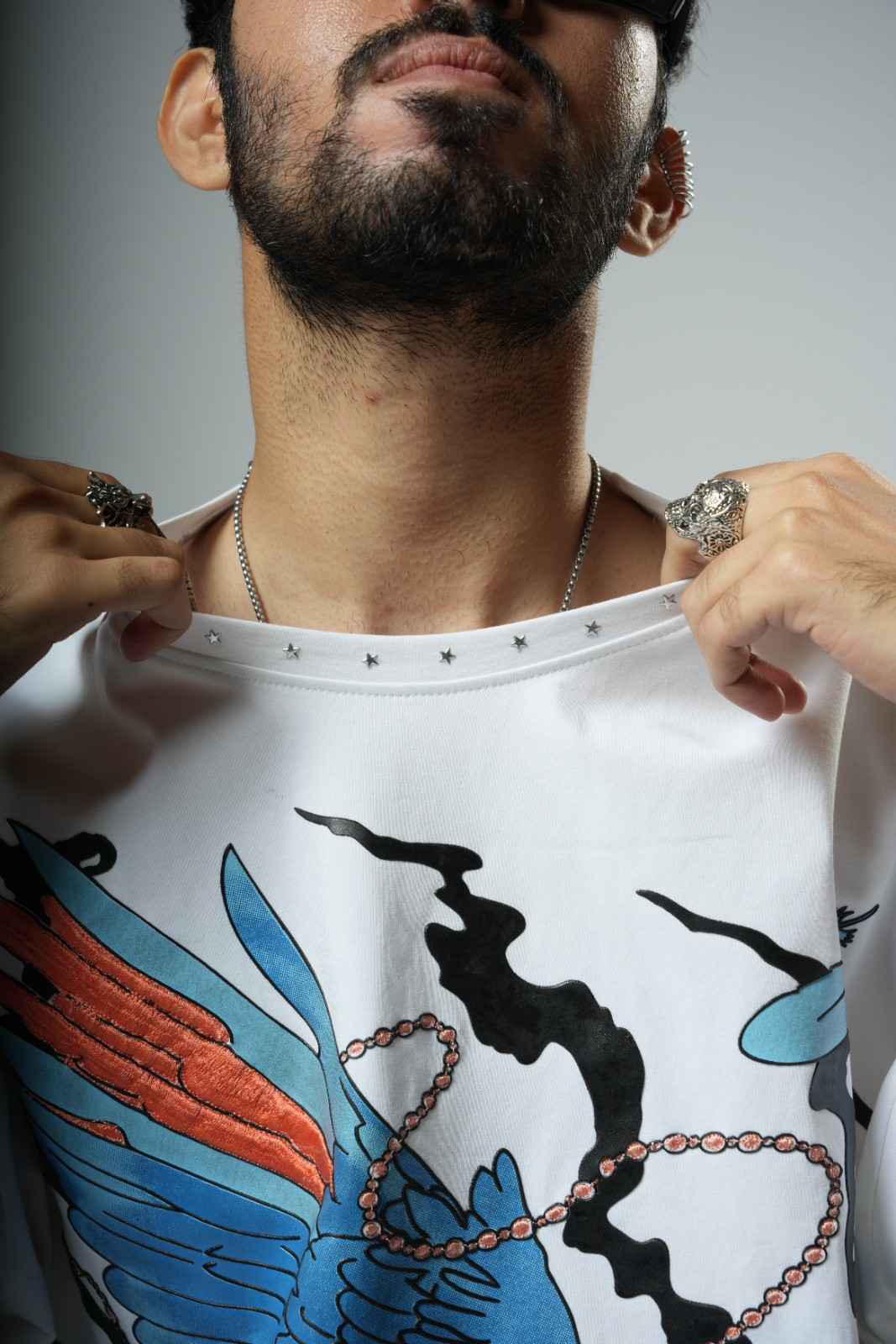 Man wearing a white shirt with colorful designs, holding it open to reveal a plain background.