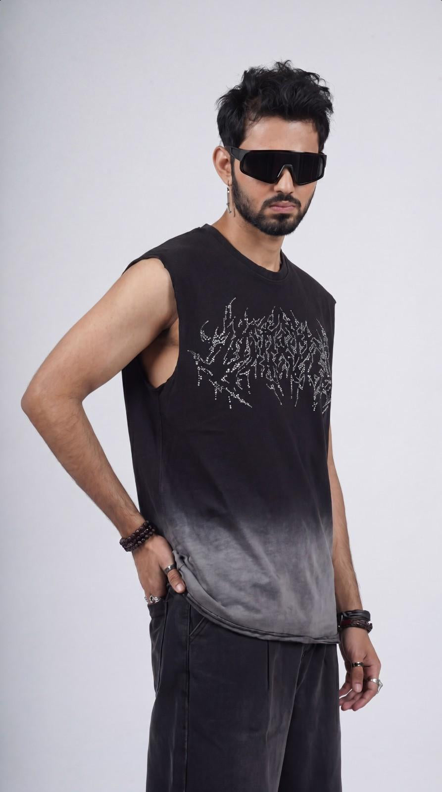 Man wearing a black sleeveless shirt with a design, sunglasses, and dark pants on a white background
